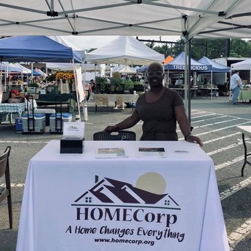 HOMECorp employee standing at a table with the HOMECorp logo on the tablecloth.  